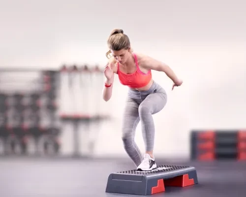 Femme blonde exécutant un cours de step dans la salle de cours collectifs à la salle de sport Fitness Morteau.